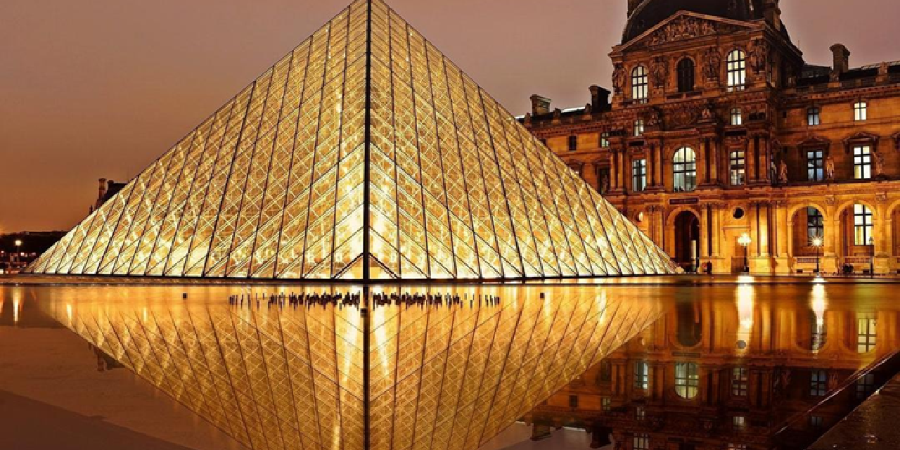The illuminated Louvre Pyramid at night with its reflection in the water in Paris, France.