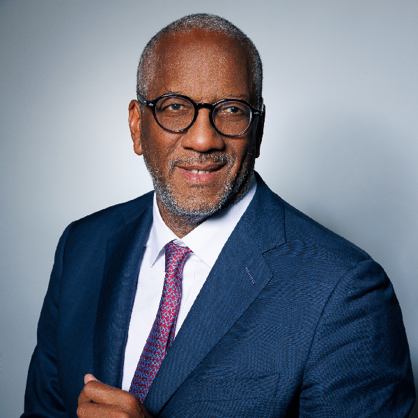 Professional portrait of a senior business consultant wearing a blue suit, white shirt, and red tie, smiling at the camera.